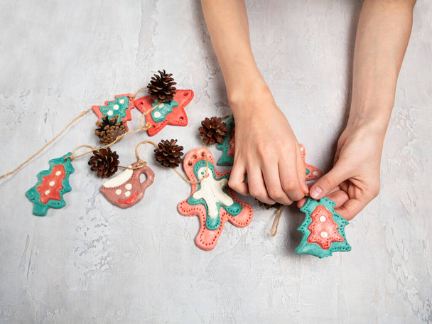 Children's hands are holding a homemade garland. Gingerbread men are made of salted dough, cones. Light background. Homemade home decoration for Christmas. - Foto, imagen
