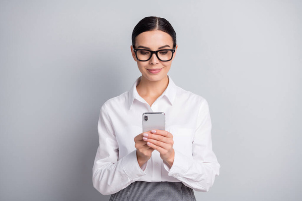 Photo of calm business lady hold telephone look screen wear eyeglasses white shirt isolated grey color background - Fotó, kép