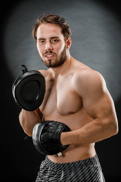 The boxer is a fighter, looking angrily at the camera. Young Caucasian male fitness model isolated on black background. - Photo, Image
