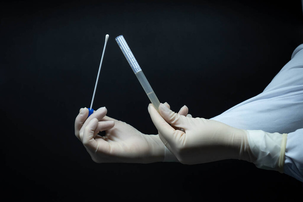 Arzthände mit weißen sterilen Handschuhen, die den PCR-Test für Covid-19 im Profil halten, schwarzer Hintergrund - Foto, Bild