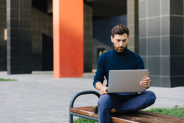 Handsome man sitting on bench and working on laptop - Photo, Image