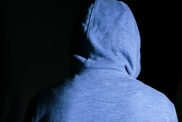 sad man in hood cover face with hands isolated in black. - Foto, imagen