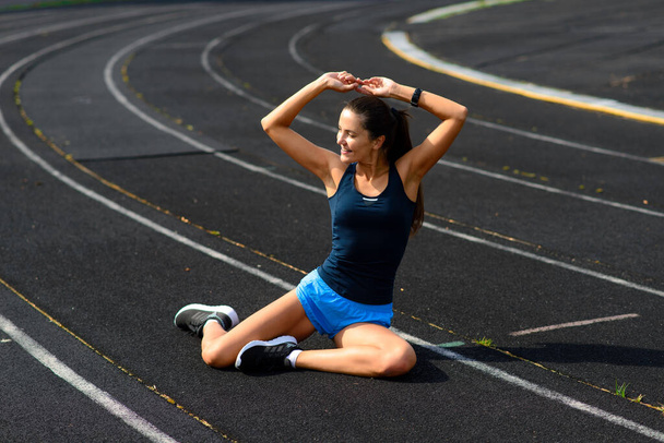 Healthy young woman warming up stretching her arms in the stadium outdoor, jogging session in park. - Foto, immagini