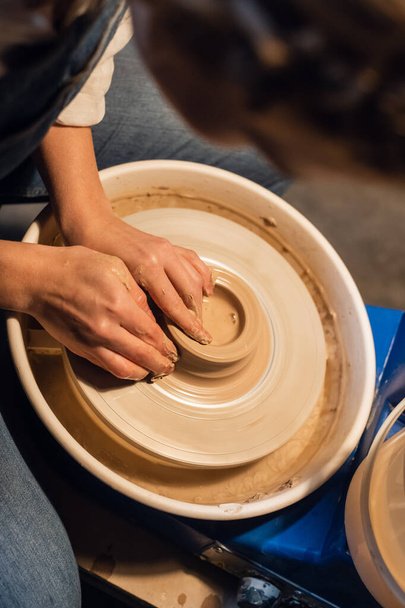 mooie handen van een jonge pottenbakkers meisje in het proces van het modelleren van een pot in de werkplaats. - Foto, afbeelding
