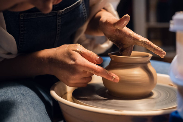 Nahaufnahme der Hände eines Töpfers beim Modellieren einer Vase aus Ton auf einer Töpferscheibe in der Werkstatt. - Foto, Bild