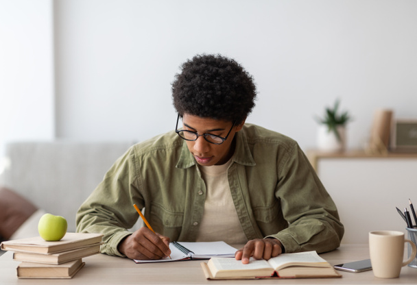 Vzdálené učení. Student černé vysoké školy si dělá poznámky z učebnice, doma studuje během propuknutí koronaviru - Fotografie, Obrázek