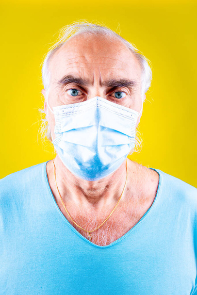 Старший носит медицинскую маску изолированы на желтом фоне, глядя на камеру защиты от эпидемии гриппа, аллергии на пыль, Covid-19 - Фото, изображение