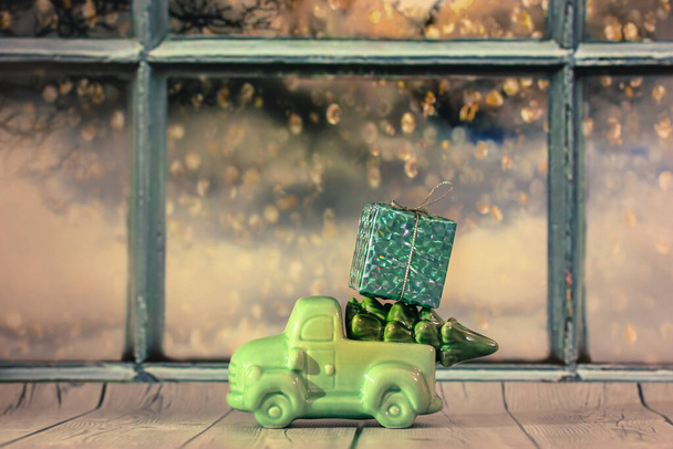Hračkové auto s vánočním stromečkem a krabicí dárků na střeše u okna - Fotografie, Obrázek