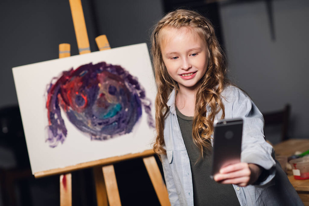 une jeune jolie artiste prend un selfie sur fond de peinture dans le Studio. - Photo, image