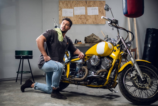 Un joven moderno con una camiseta y jeans se dedica al diagnóstico de bicicletas en un taller de reparación o garaje. - Foto, Imagen