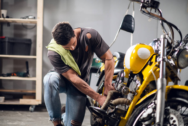 Mladý opravář sportovních motocyklů v garáži nebo dílně pracuje na žlutém kole. - Fotografie, Obrázek