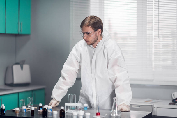 Υπέροχη μέρα στο εργαστήριο. Νεαρός άνδρας χημικός με προστατευτικά γυαλιά που εργάζεται στο εργαστήριο - Φωτογραφία, εικόνα