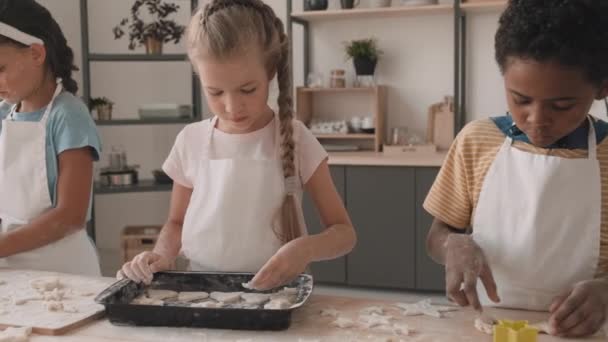 Slow mo of multiethnic boys and girls preparing cookies in shapes of hearts and stars. African, Caucasian and Mixed-Race children wearing aprons cooking together in kitchen - Footage, Video
