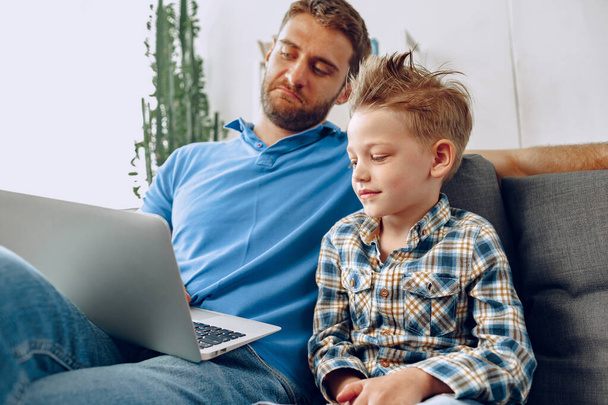 Отец и сын сидят на диване и смотрят что-то на ноутбуке - Фото, изображение