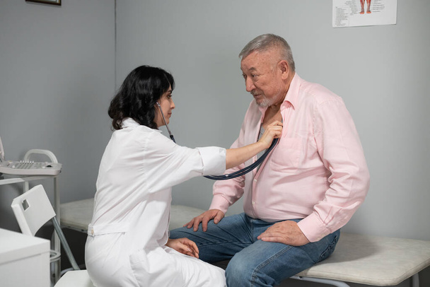 Un vecchio che si fa controllare il battito cardiaco dal dottore con uno stetoscopio - Foto, immagini