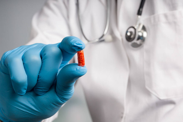 La mano del medico nei guanti medici presenta una pillola di medicina rossa  - Foto, immagini