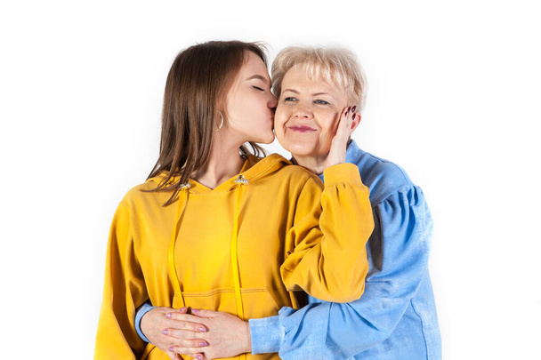 Hija joven besando a su anciana madre sobre fondo blanco. Familia cariñosa - Foto, imagen