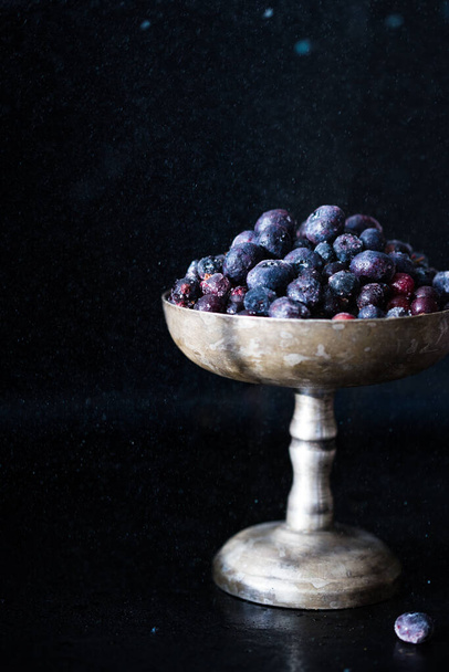 Frozen berries fell out of a vintage bowl on black background. - Foto, Imagen