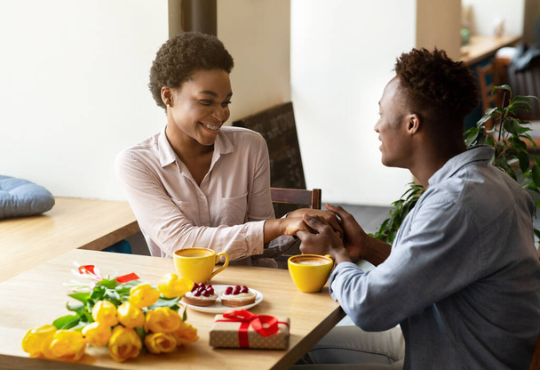 Liefdevolle zwarte man feliciteert zijn vriendin met vakantie, geven haar bloemen en cadeau in stedelijke cafe - Foto, afbeelding