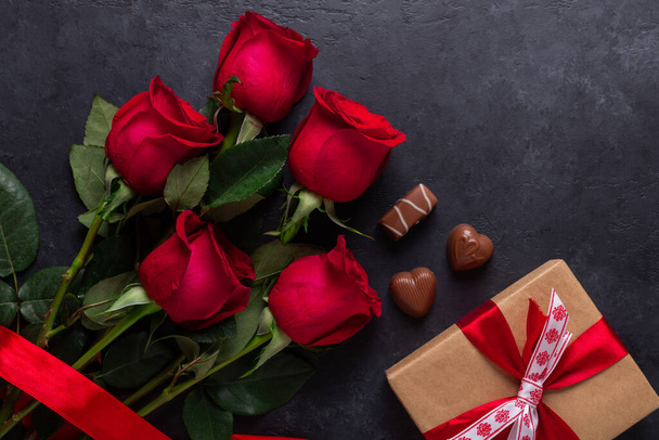 Red rose flowers bouquet, gift box, chocolate sweets on black stone background Valentine's day greeting card Copy space Flat lay - Fotografie, Obrázek
