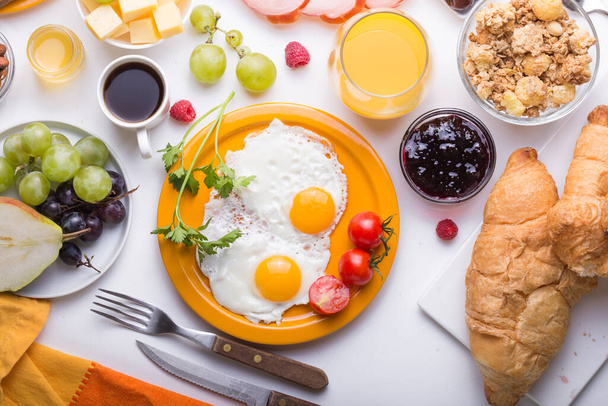 Homemade breakfast with sunny side up fried egg croissant toast coffee fruits vegetable and orange juice in top view with copy space. Delicious homemade American breakfast concept for background - Photo, Image