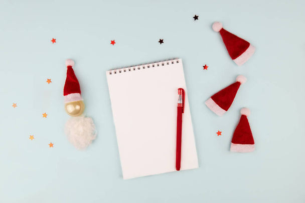 Christmas composition, wish list concept. Notebook with pen, gift, decoration and hats Santa Claus on light background. Flat lay, top view, copy space - Photo, Image
