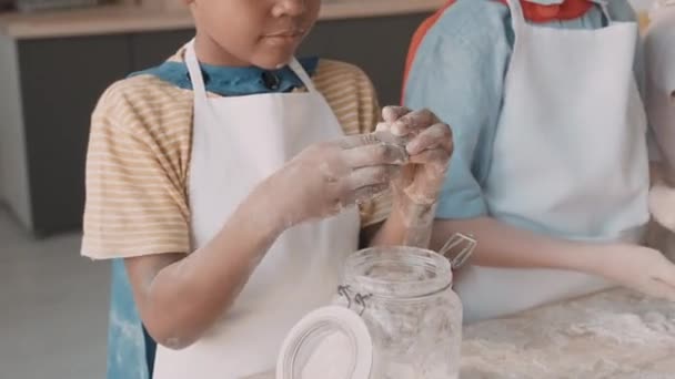 Medium close-up of African school boy sculpting dough, standing at table in kitchen near friends. Children wearing aprons, cooking together - Footage, Video