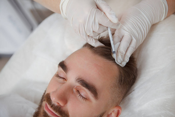 Zbliżenie młodego atrakcyjnego mężczyzny otrzymującego zastrzyki do włosów od profesjonalnego kosmetologa - Zdjęcie, obraz