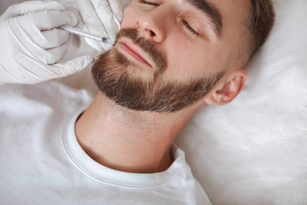 Cropped close up of a bearded man getting face filler injections into wrinkle areas - Photo, image