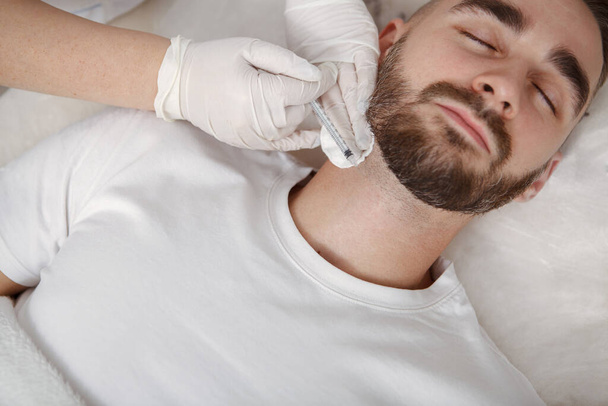 Cropped shot of a beautician injecting facial filler into neck wrinkles of a male client - 写真・画像