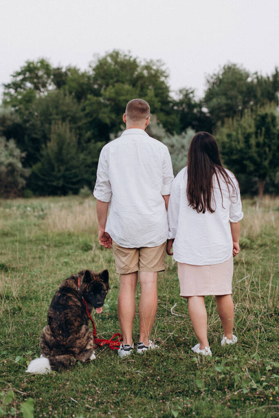 Американская собака Акита для прогулки с парнем и девушкой на зеленой прерии - Фото, изображение