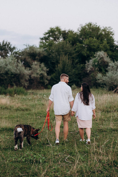 American Akita dog for a walk with a guy and a girl on the green prairie - Φωτογραφία, εικόνα