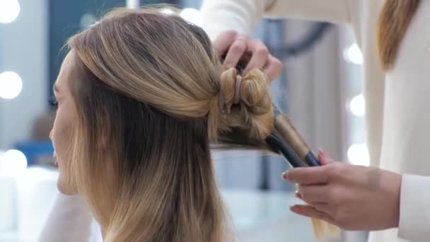 Junge brünette Frau Friseur macht Styling auf den langen Haaren des blonden Mädchens - Filmmaterial, Video