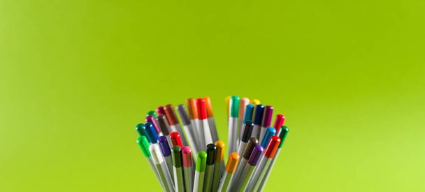 Un conjunto de lápices de colores para la creatividad en casa en una taza sobre un fondo verde claro, vista lateral. Espacio para texto, formato ancho. - Foto, imagen