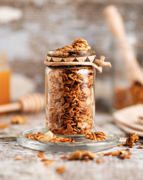 granola fait maison avec des noix et du miel dans un bocal en verre sur un vieux fond en bois clair - Photo, image