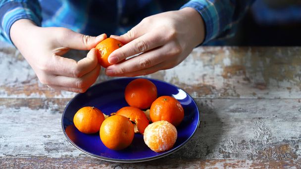 Men's hands are peeling mandarin. Tangerines on a plate. Skins of tangerine. - Foto, immagini