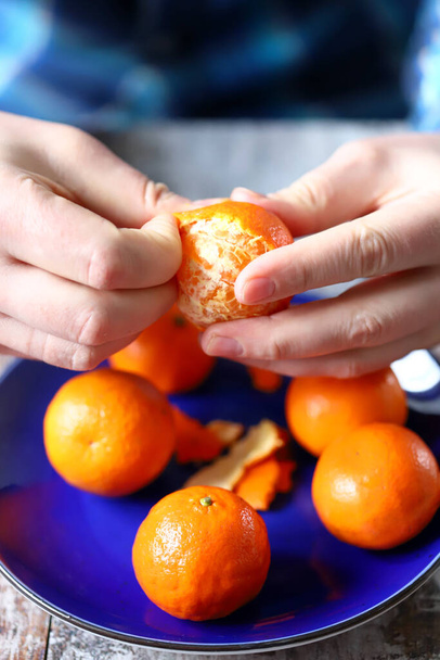 Un homme épluche des mandarines. Des tangerines sur une assiette bleue. Les mains du chef éplucher les mandarines. - Photo, image