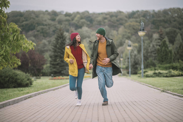 Young couple running in the park and looking cheerful - Фото, зображення