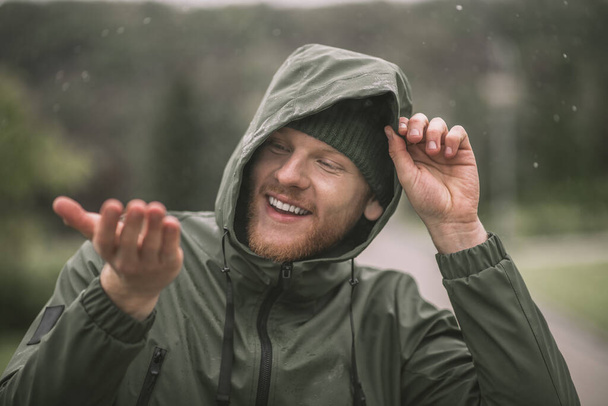 Man in a green coat catching rain drops and smiling - Foto, Imagem