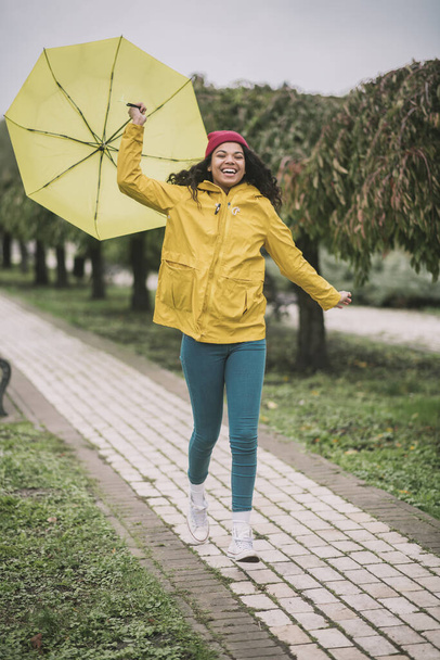 Cute mulatta with yellow umbrella looking joyful - Foto, imagen