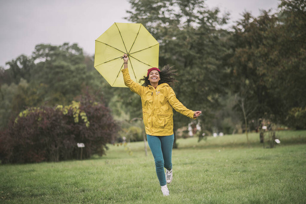 Cute mulatta with yellow umbrella running and having fun - Foto, imagen
