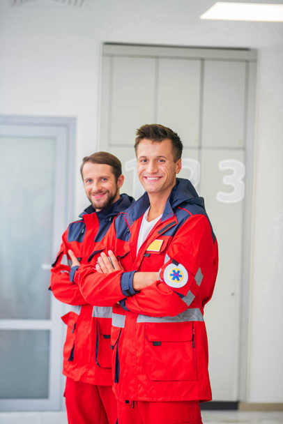 Two medical workers in red uniform smiling and feeling confident - Foto, afbeelding