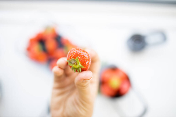 Mano femenina sosteniendo una fresa fresca por encima de más bayas - Foto, imagen