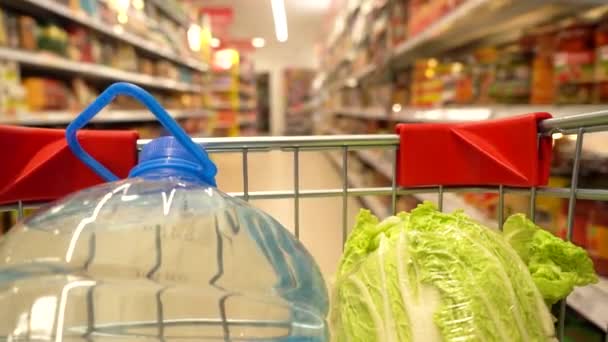 A grocery cart in a supermarket moves down the aisle between the shelves. Inside view of the cart - Video