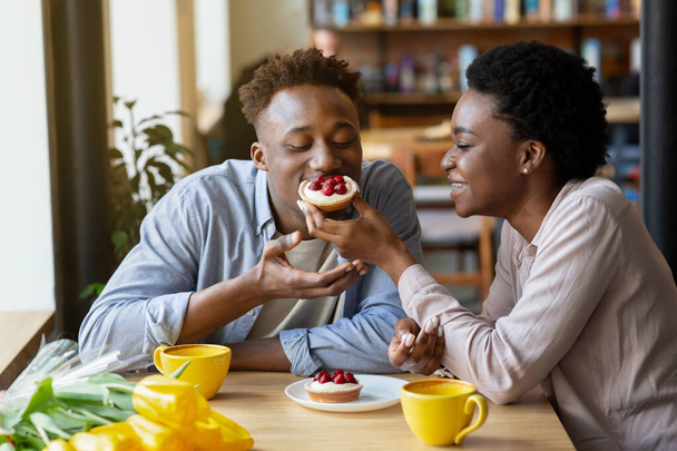 Прекрасна чорна жінка годує смачний ягідний тартлет своїм хлопцем у затишному міському кафе
 - Фото, зображення