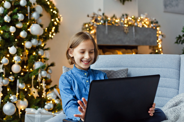 Молодая девушка удаленно общается с помощью компьютера. Новогодние поздравления через Интернет. Рождественская атмосфера - Фото, изображение