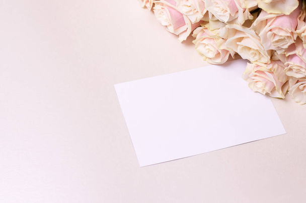 Beautiful bouquet of many roses on a beige background with a white card and place for text. Concept for love, birthday, holiday, celebration, invitation. Women's day theme. Nobody.  - Photo, Image