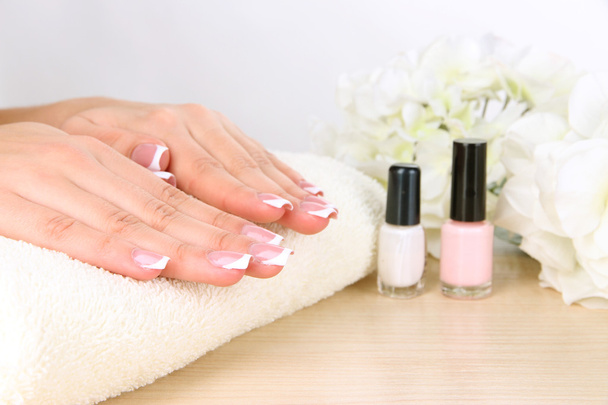 Beautiful woman hands with french manicure and flowers on table on white background - Photo, Image