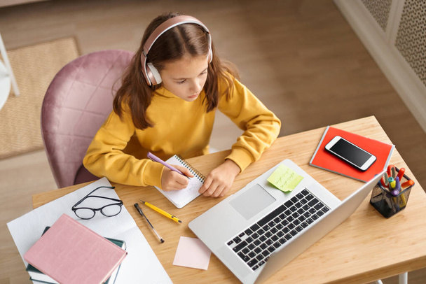 Draufsicht eines jungen Mädchens mit Kopfhörern, das am Schreibtisch in ihrem Zimmer Hausaufgaben macht, Laptop, Internet benutzt und Online-Unterricht bei einem Fernlehrer hat. Hausaufgabenbetreuung während der Covid-19-Quarantäne - Foto, Bild