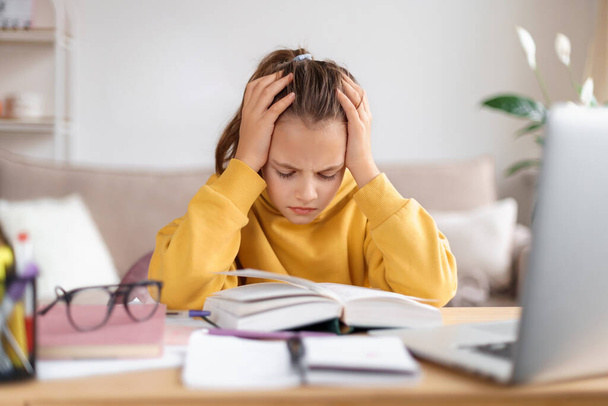 Exhausted schooler girl suffering from doing homework, tired from studying at home, getting ready before exams, stressed with difficult task, reading book, using laptop. Home education, homeschooling - Photo, Image